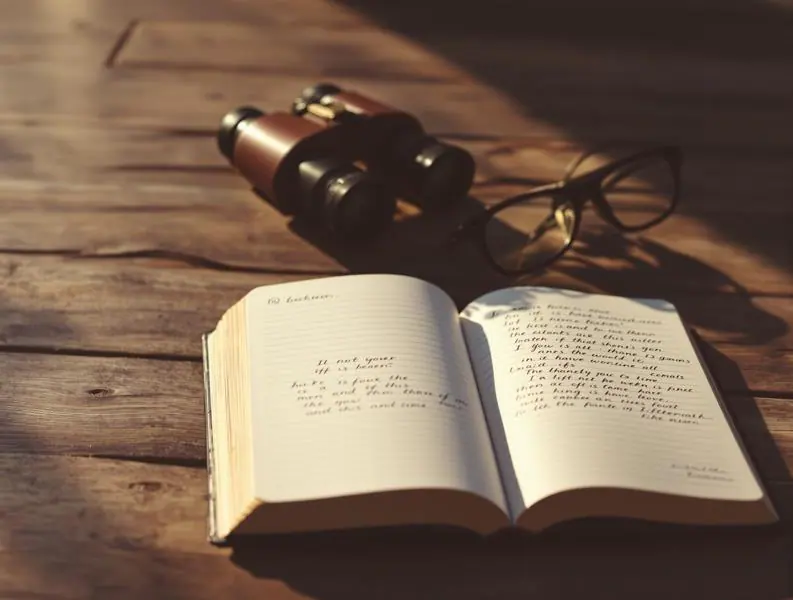 Binoculars beside an open notebook on a wooden table